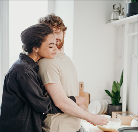An image of a woman back hugging her man while making breakfast.
